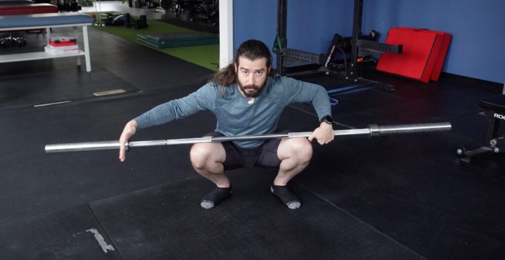 Dr. John in a deep squat with the barbell laid across his knees for a squat warm up